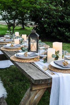 an outdoor table set with candles and place settings