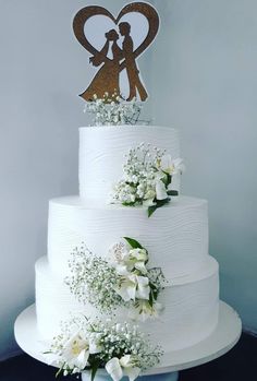 a wedding cake with white flowers and a couple on top