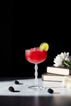 a red cocktail sitting on top of a table next to a book and some flowers