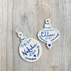 two blue and white ceramic ornaments hanging from hooks on a wooden surface, with the word naddel written in cursive writing