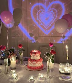 a table topped with a cake and candles next to balloons in the shape of a heart