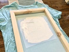 an unfinished piece of paper is displayed in a shadow box on the floor next to a t - shirt