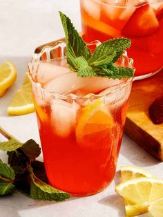 two glasses filled with lemonade and mint on top of a table next to sliced lemons