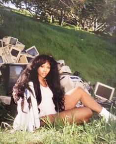 a woman sitting in the grass next to a pile of computers