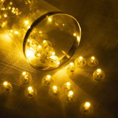 a glass jar filled with yellow lights on top of a table covered in plastic balls