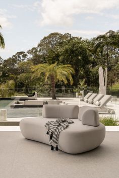 a white couch sitting on top of a cement floor next to a swimming pool and palm trees