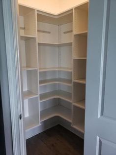 an empty walk in closet with white shelving and wood flooring on the side