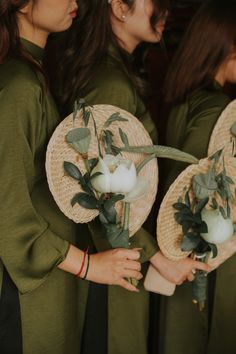 three women in matching green dresses hold straw hats with white flowers and greenery on them