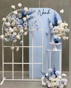 a white and blue wedding arch with flowers on the side, next to it are two vases