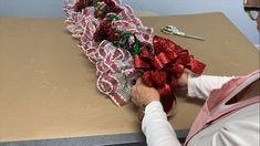 a woman is making christmas decorations with red and green ribbons on a brown table next to a pair of eyeglasses