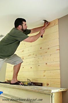 a man holding a hammer while standing on top of a wooden shelf next to a wall