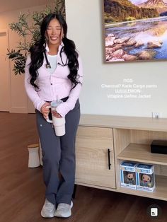 a woman standing in front of a tv holding a cup and smiling at the camera