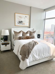 a bedroom with a large window and a white bed in front of a painting on the wall