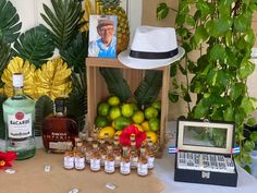 a table topped with bottles of alcohol and fruit next to a laptop computer on top of a desk