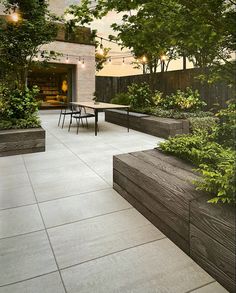 an outdoor dining area with tables and benches surrounded by greenery, trees and shrubs