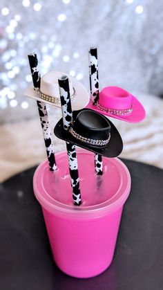 three straws with black and white hats on them sitting in a pink cup filled with candy