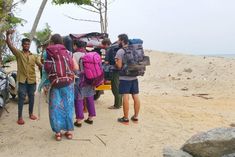 group of people with backpacks standing in front of a vehicle on the side of a beach