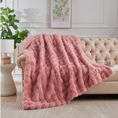 a couch with a pink blanket on top of it next to a potted plant