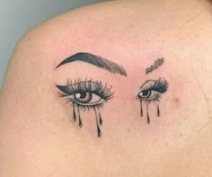 a woman's shoulder with an eye and lashes tattoo on her upper arm, which has teary tears