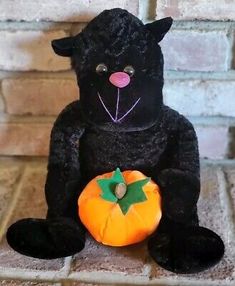 a black stuffed animal holding a pumpkin on a brick floor in front of a brick wall