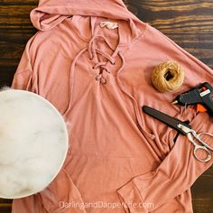 an orange shirt and some scissors on a wooden table with yarn, pliers and other crafting supplies