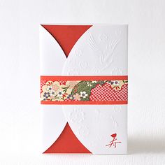 a red and white card with an orange ribbon around it's edge on a white surface