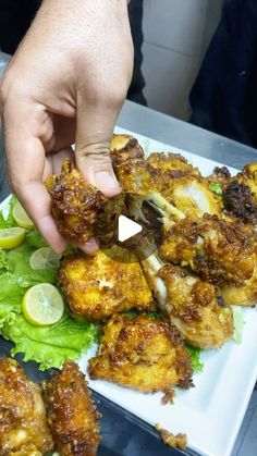 someone is picking up some fried food from a white plate with lettuce and lemon wedges