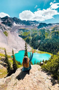 a woman sitting on top of a mountain with her arms in the air