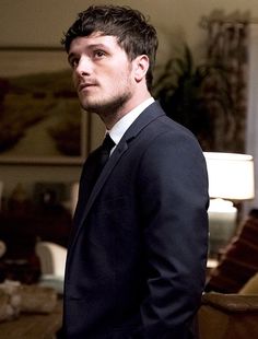 a man in a suit and tie standing in a living room looking off into the distance