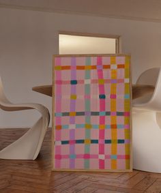 an abstract painting on display in a room with white chairs and a wooden table next to it