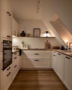 an attic kitchen with white cabinets and wood flooring is lit by the light coming through the window