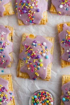 purple frosted desserts with sprinkles on white parchment paper lined up