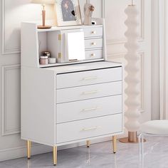 a white dresser sitting next to a lamp on top of a wooden table in a room