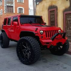 a red jeep parked in front of a building on the side of the road with black wheels