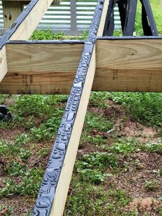 the bottom section of a wooden structure with metal bars attached to it and grass growing in the background