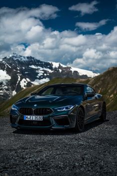 a blue car parked on top of a gravel road next to snow covered mountains and clouds