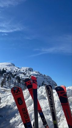 several skis are lined up in the snow near a mountain side with a blue sky