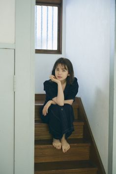 a woman sitting on the stairs in front of a window with her hand under her chin