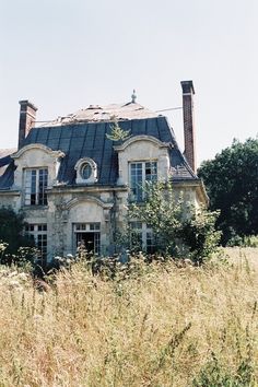 an old abandoned house sitting in the middle of a field with tall grass around it