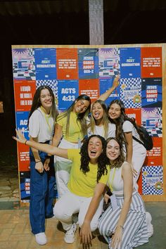 a group of young women posing for a photo in front of a wall with posters on it