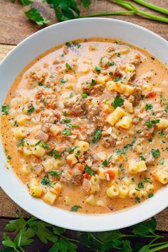 a white bowl filled with pasta and meat soup on top of a wooden table next to parsley