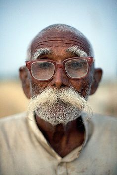 an old man with glasses and a white beard is looking at the camera while standing in a field