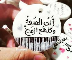 a person holding a white button with arabic writing on it and hearts in the background