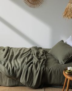 an unmade bed with green sheets and pillows on it, next to a small side table