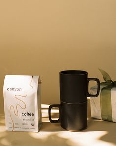 two coffee mugs next to each other on a table with a bag and box