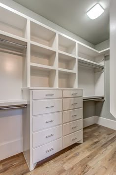 an empty walk in closet with white shelves and drawers on the wall, along with hardwood flooring