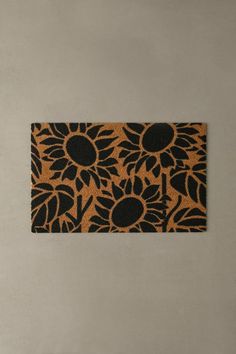 an orange and black door mat with sunflowers in the center on a gray wall