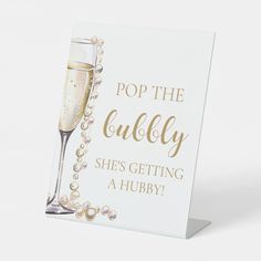 a card with a glass of champagne and pearls on the bottom reads pop the bubbly she's getting a hubby