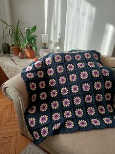 a crocheted blanket is sitting on a chair next to a potted plant