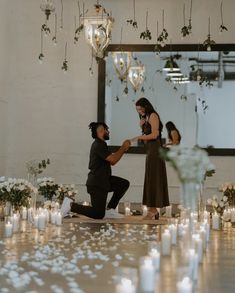 a man kneeling down next to a woman on top of a wooden floor surrounded by candles